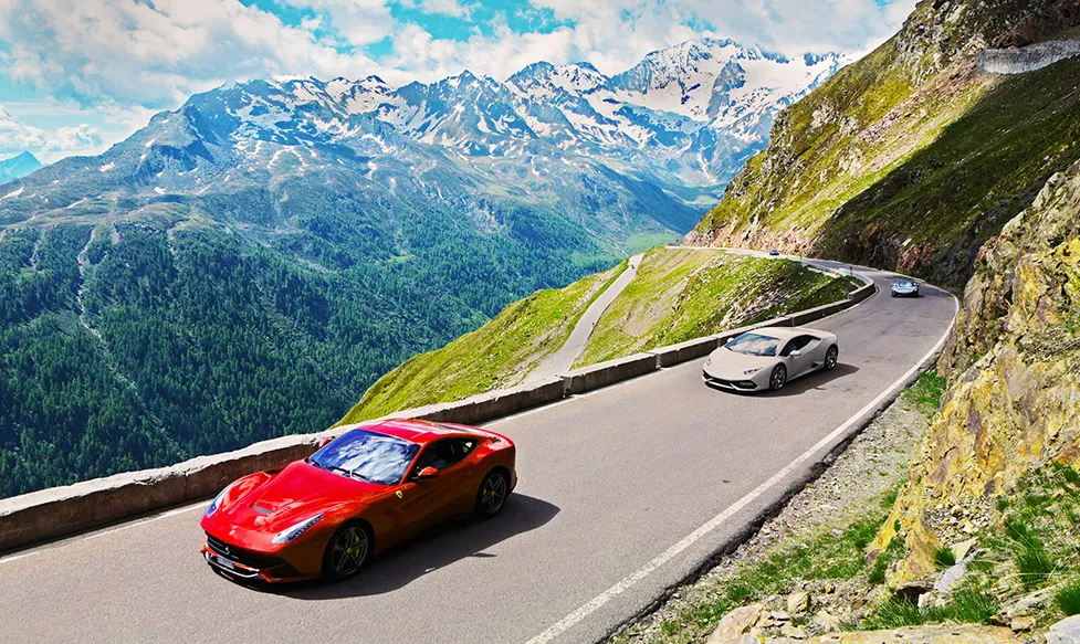 A red Ferrari 812 Superfast leads a white Lamborghini as they ascend the Stelvio Pass, Italy