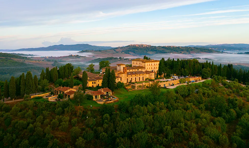 an elevated view of Castello di Casole, Tuscany. The castle’s surrounding hills are shrouded in light fog
