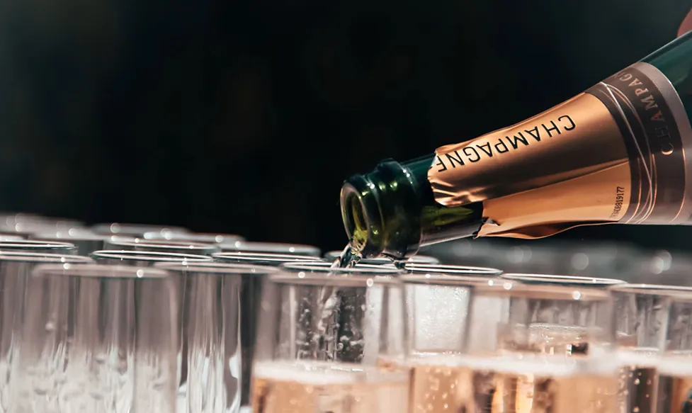 A close-up shot of the neck of a Champagne bottle as it is poured into flutes
