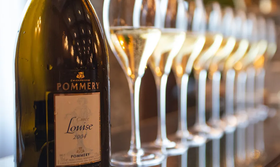 A recently-poured bottle of Pommmery champagne sits in the foreground in front of half-filled champagne glasses