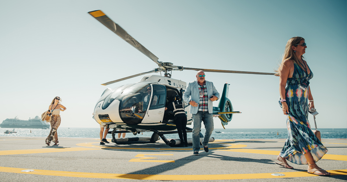 Three luxury tour guests in fashionable outfits disembarking from a helicopter 
