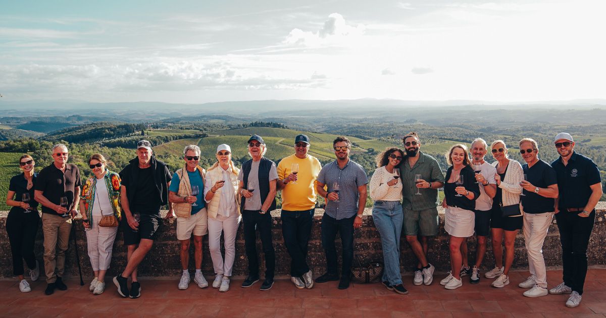 A group of luxury tour guests pose in front of a backdrop of rolling hills in Europe