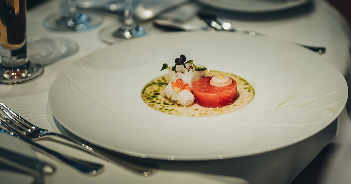 A delicately plated fish dish on a large white plate with artistic engravings.