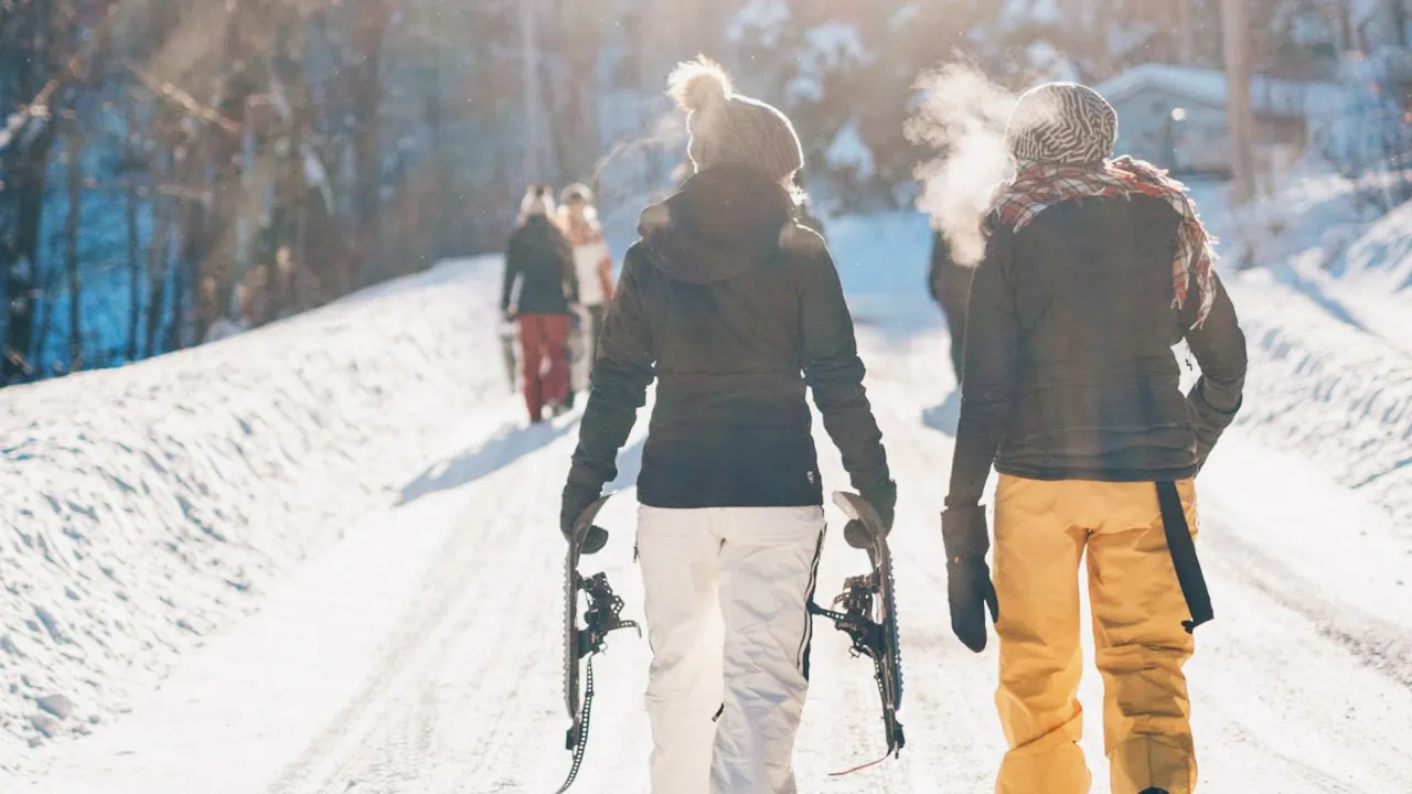 Two people surrounded by snow, walking away from the camera with ski equipment