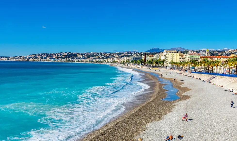 A gravel beach on the French Riviera with brilliant blue water and a clear blue sky