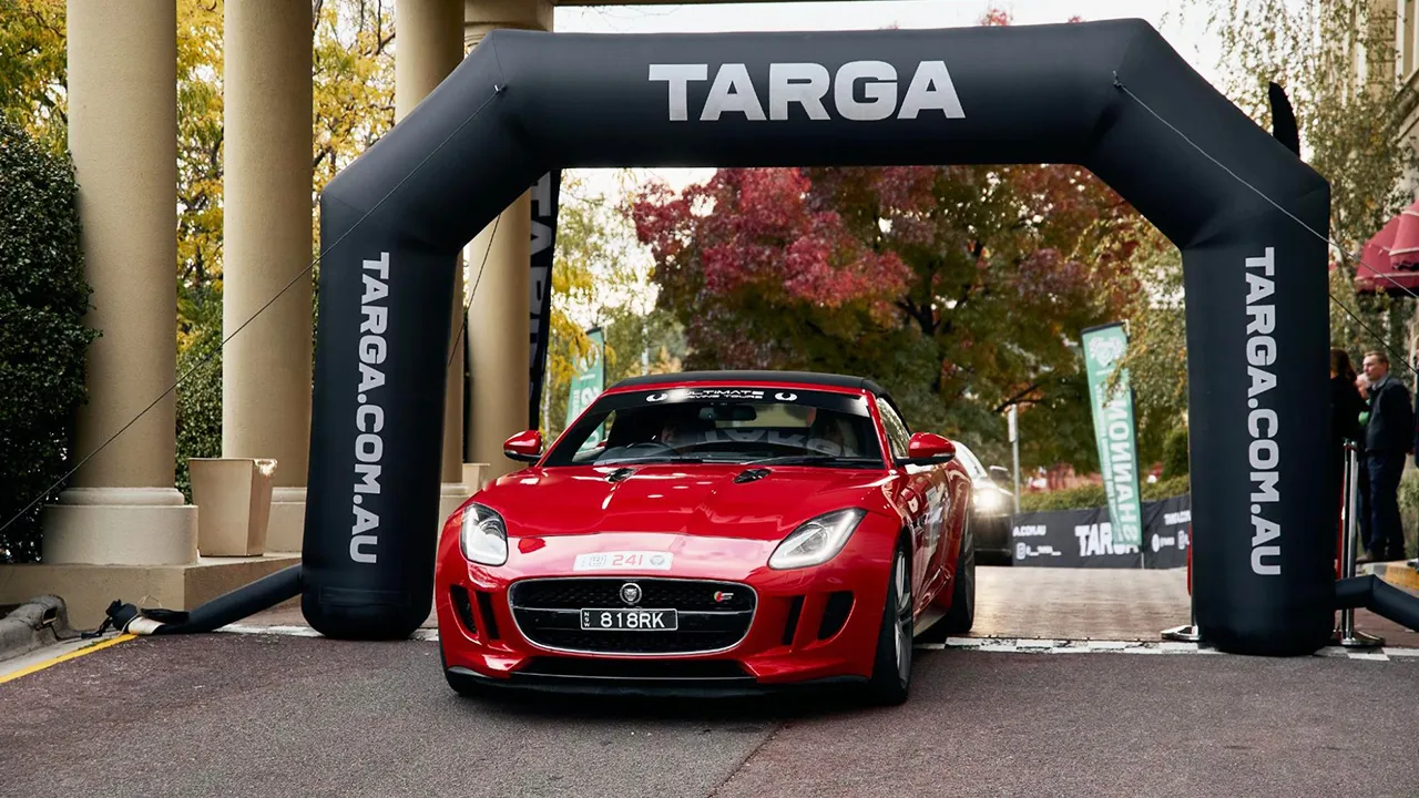 A red supercar driving through the Targa Tasmania event banner