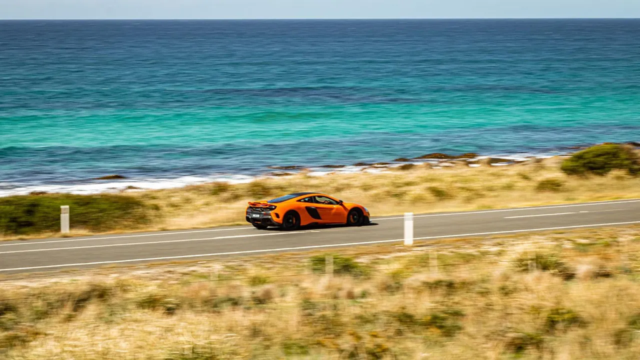 Orange supercar racing along the coast of Tasmania in the annual Targa Tasmania rally