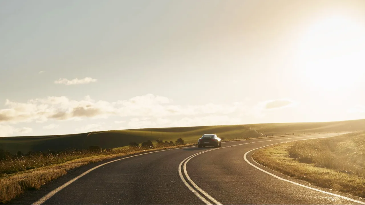 A supercar pictured cresting a hill driving into the afternoon sun