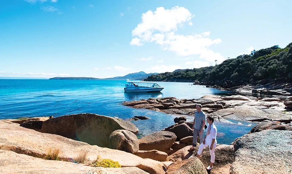 A couple look out to sea as they stand on rocks in Coles Bay, Australia