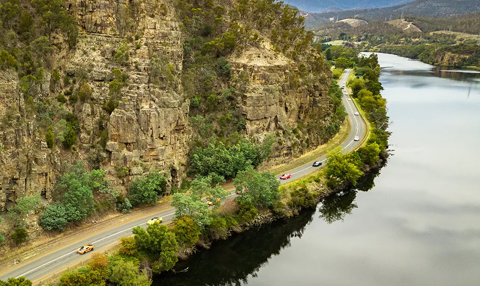 Supercars drive a section of dramatic coastal road next to steep cliffs in Australia